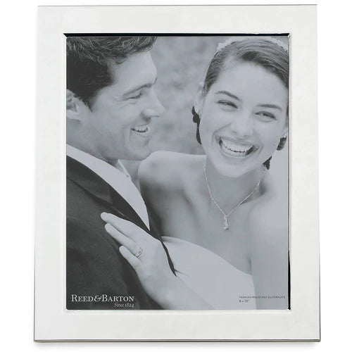 A black-and-white photo of a smiling bride and groom in wedding attire is displayed in the Reed & Barton - Brass Frame - 1480GA, a simple and tarnish-resistant silver-plated frame by Reed & Barton. The bride laughs as the groom looks at her fondly.