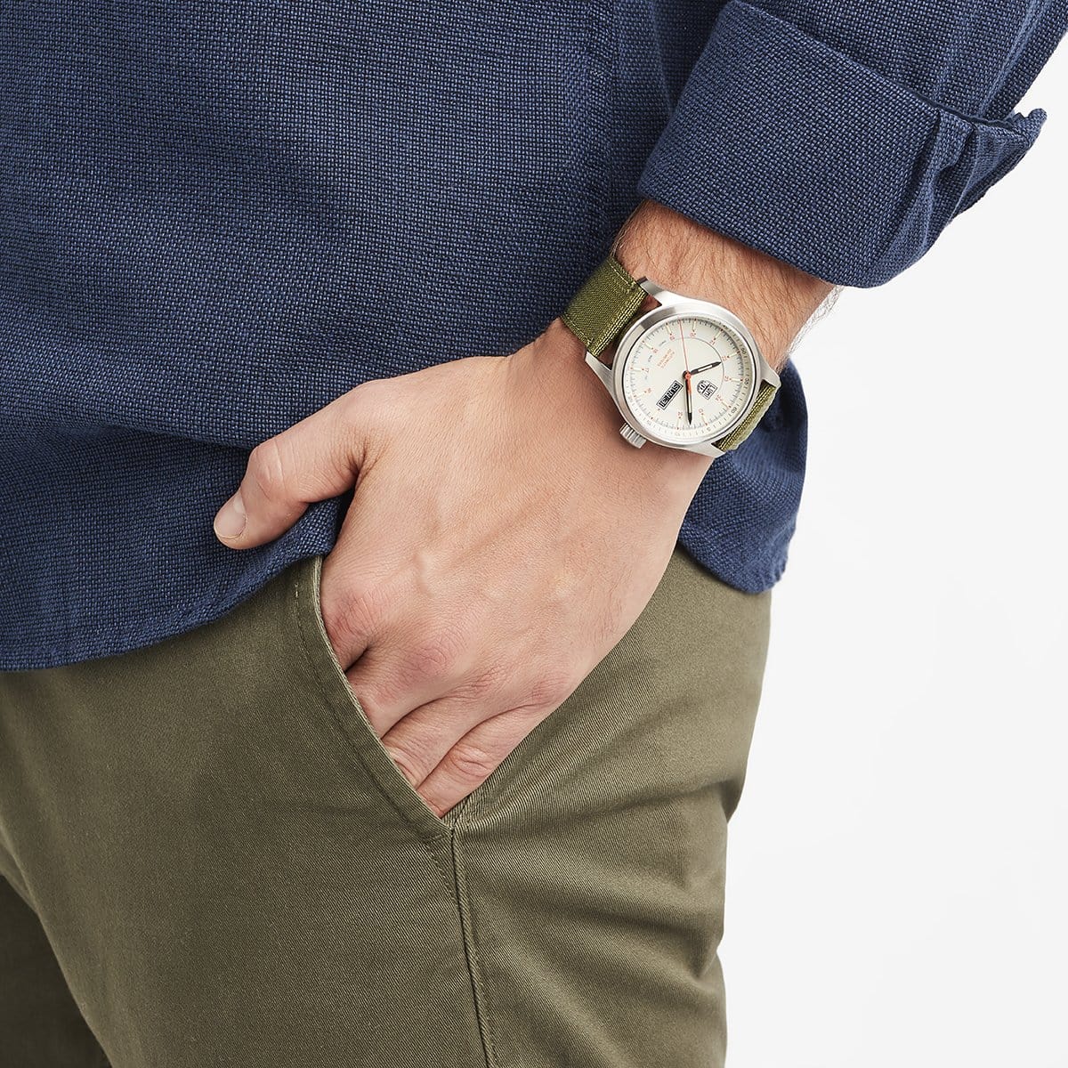 A person wearing the Luminox Atacama Field Automatic XL.1907.NF watch and a blue textured shirt with khaki pants stands with one hand in their pocket.
