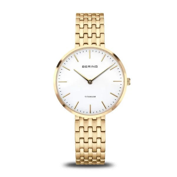 The Bering Watch - Titanium Womens Gold (19334-334) features a white face, minimal gold markers, slim gold hands, and a gold metal link band. This elegant hypoallergenic ladies watch by Bering is shown against a white background.