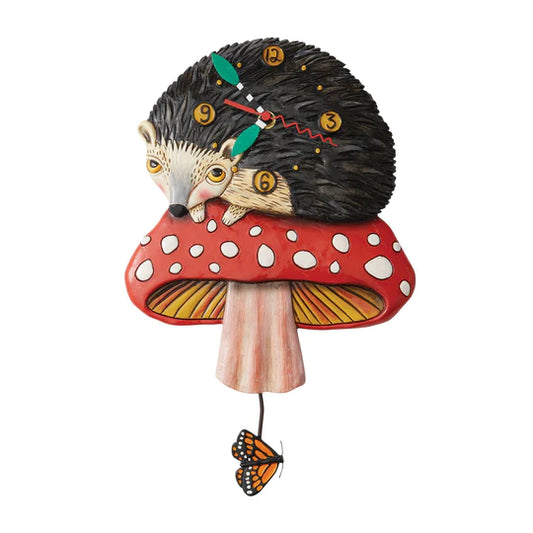 The Enesco Allen Designs Clock - Hank the Hedgehog (6012910) features a whimsical hedgehog curled on a red-and-white mushroom, with a clock face on its back and monarch butterfly pendulum—an ideal charming gift or unique decor piece.