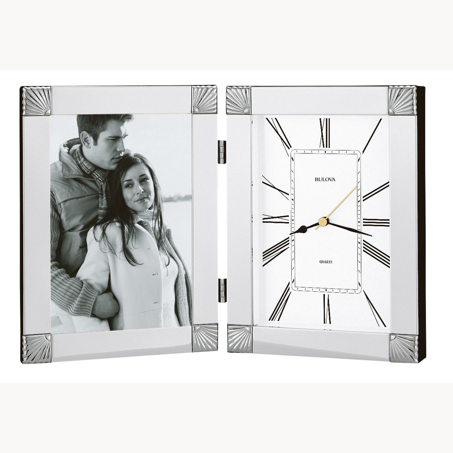 A framed photo of a couple in winter clothing stands beside the elegant Bulova Ceremonial Clock (B1254), both set in a hinged chrome finish display with Roman numerals and a sleek engraving plate.