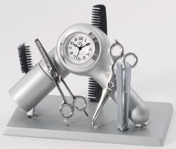 The Sanis Mini Clock - Silver Hair Dresser (CK365) by Sanis Enterprises features a silver hair dryer-shaped clock, surrounded by scissors, combs, and brushes, all elegantly displayed on a rectangular stand.