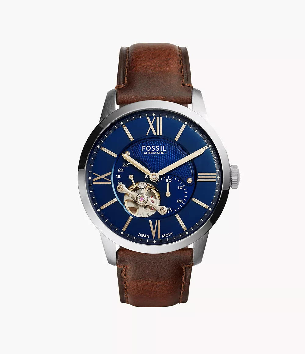 The Fossil Townsman Automatic ME3110 features a blue face with visible gears, gold-tone markers, Roman numerals at 12 and 6 o’clock, a brown leather strap, and a stainless steel case.