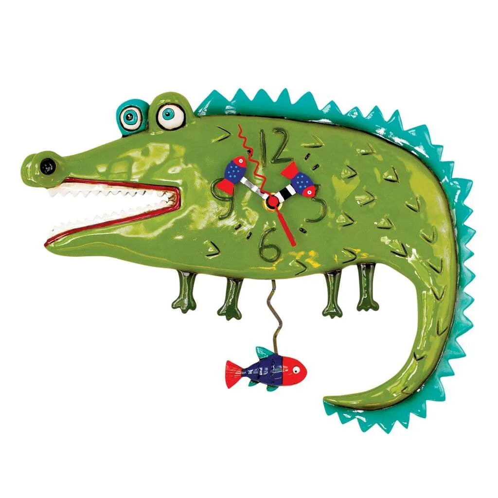 The Enesco Allen Designs Clock - Later Gator (P1998) is a hand-painted green alligator wall clock with big eyes, a wide open mouth, red and blue fish hands, and a red fish pendulum hanging from its tail.