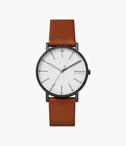 The Fossil Skagen Watch - Signatur - SKW6374 features a white dial, black markers, blue and orange hands, and a brown leather strap—offering a simple, modern design perfect for everyday wear.