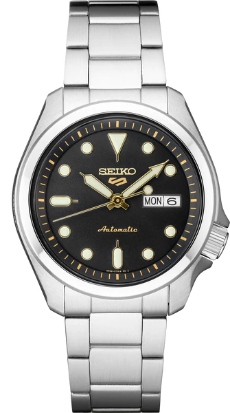The Seiko Watch - SRPE57 - Seiko 5 Sports by Seiko features a silver case, black dial with gold accents, round hour markers, day-date display set to MON 6, and a metal link bracelet for a timeless look.