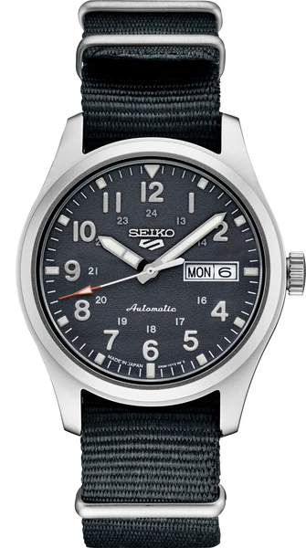 The Seiko SRPG31 from the Seiko 5 Sports Collection features a black dial with white Arabic numerals, day-date at 3 o’clock, silver hands, 24-hour markings, and a durable black nylon strap.