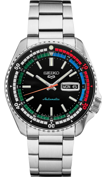 The Seiko 5 SRPK13 55th Anniversary Special Edition features a stainless steel band, black dial, multicolored (red/blue/green) bezel, and day/date display at 3 o’clock. Brand: Seiko.