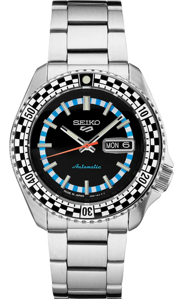 The Seiko 5 Sports SRPK67 automatic watch by Seiko features a stainless steel band, black dial, blue and white checkered bezel, and day-date display set to Monday the 6th. Silver hands pair with a striking orange second hand.