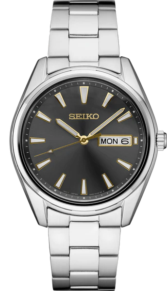 The Seiko Essentials Collection SUR343 features a stainless steel silver band, black dial, gold hour markers and hands, plus a day-date display at 3 o’clock showing MON 6.