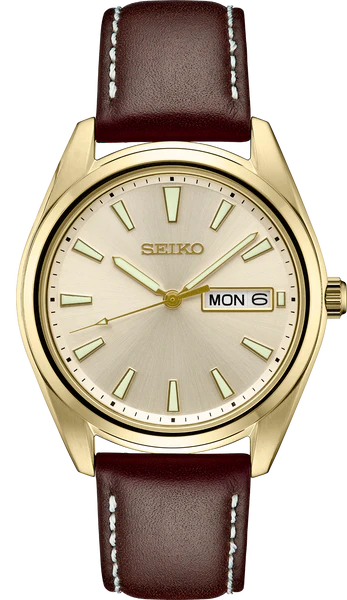 The Seiko Watch - Essentials Collection - SUR450 is a mens gold dress watch with a cream dial, gold markers and hands, brown leather strap with white stitching, and a day-date display at 3 o’clock.
