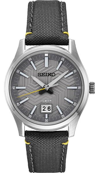 The Seiko Watch - Essentials - SUR543 by Seiko features a silver case, grey geometric dial, white markers, yellow seconds hand, and a black fabric strap with yellow stitching. Reliable quartz movement. Date window shows the 26th.