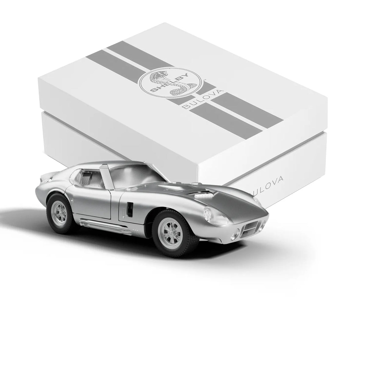 A silver die-cast toy sports car in front of a white Bulova SHELBY® Racer Chronograph - 96K118 presentation box with two grey racing stripes.