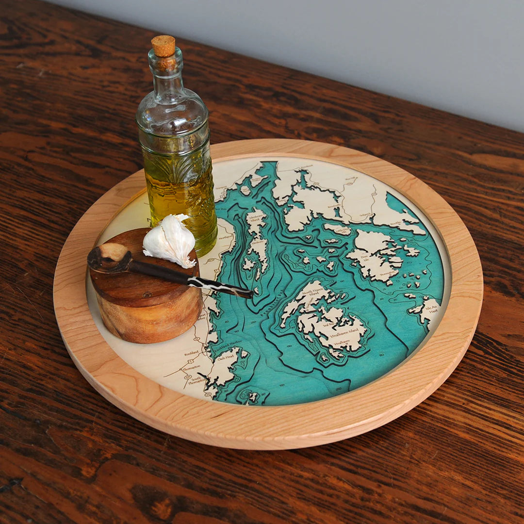 The Lake Art Lake Gift - Galway Lake Multi Depth Lazy Susan displays a blue and beige topographic map of Galway Lake and holds oil, a wooden container with a spoon, and garlic on a rustic wooden table.