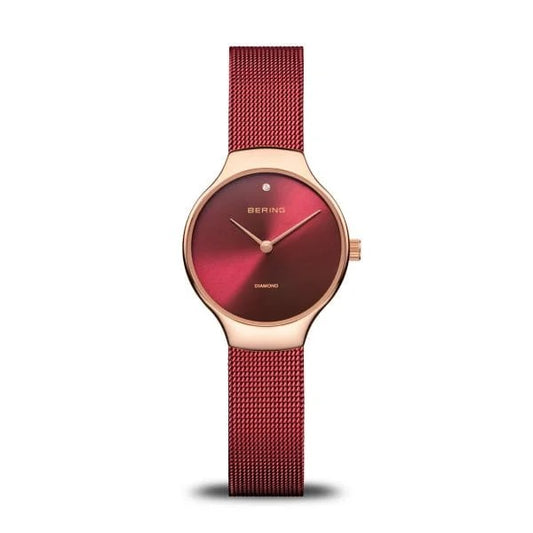 The Bering Watch - Womens Time to Care Collection 13326-Charity features a rose gold case, red mesh strap, red gradient dial with a diamond at 12 o’clock, minimal markings, and BERING below the diamond.