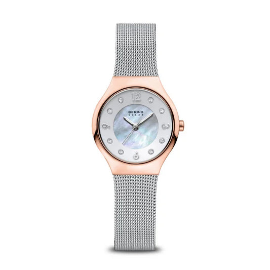 The Bering Watch - Womens Solar 14427-060 features a rose gold case, silver stainless steel mesh band, mother-of-pearl dial, crystal hour markers, and the Bering name on the face for a stylish look.