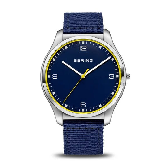 The Bering Watch - Ultra Slim Mens Blue (18342-507) by Bering showcases Danish design with a blue face, yellow ring accents, silver case, blue fabric strap, white hour markers, silver hands, and a yellow second hand at 10:08:37.