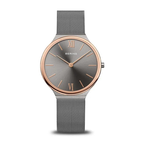 The Bering Watch - Ultra Slim Womens Brushed Grey (18434-369) by Bering features a minimalist Danish design with a gray mesh band, round gray dial, and rose gold bezel accents plus Roman numerals at 12 and 6 o’clock. No date display.