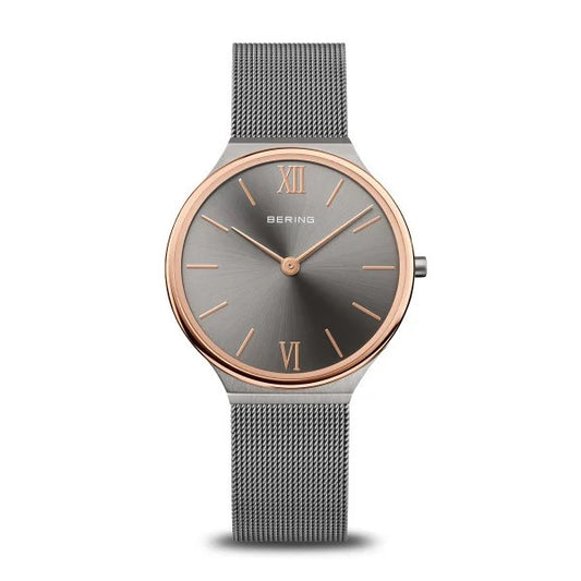 The Bering Watch - Ultra Slim Womens Brushed Grey (18434-369) by Bering features a minimalist Danish design with a gray mesh band, round gray dial, and rose gold bezel accents plus Roman numerals at 12 and 6 o’clock. No date display.