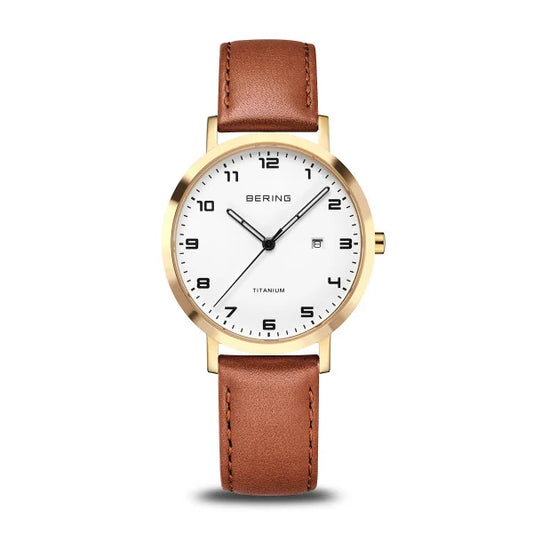 The Bering Watch - Ladies Titanium Collection - 18634-534 features a gold-rimmed case, white face with black numerals, minimalist hands, brown leather strap, and date display at three o’clock. Modern and elegant design by Bering.