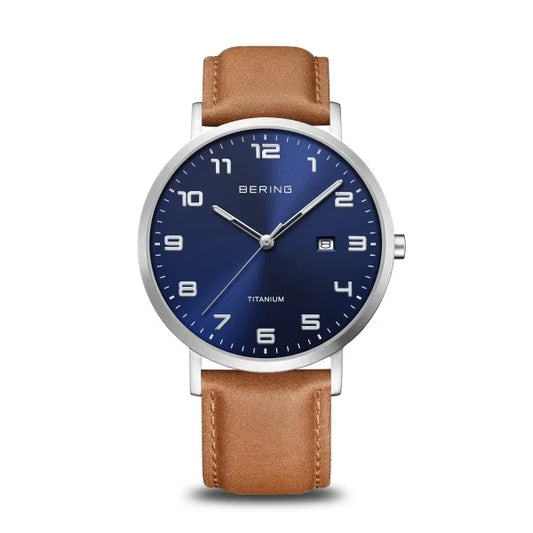 The Bering Watch - Ultra-Light Titanium Collection (18640-567) features a blue dial with white numerals, date at 3 o’clock, silver case, and brown leather strap. Shown on a white background. Brand: Bering.