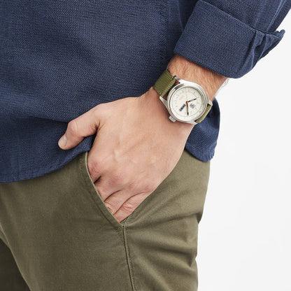A person wearing the Luminox Atacama Field Automatic XL.1907.NF watch and a blue textured shirt with khaki pants stands with one hand in their pocket.