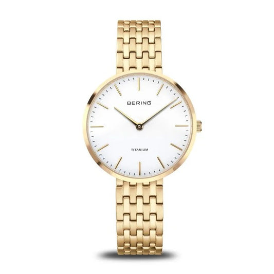 The Bering Watch - Titanium Womens Gold (19334-334) features a white face, minimal gold markers, slim gold hands, and a gold metal link band. This elegant hypoallergenic ladies watch by Bering is shown against a white background.