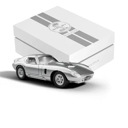 A silver Shelby Racer model car sits before a white, striped Bulova gift box—an ideal showcase for the Limited Edition Bulova Watch - SHELBY® Racer Chronograph - 96K118.