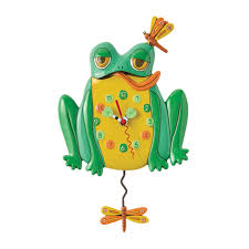 The Enesco Allen Designs Clock - Hop to it Clock (6018047) features a green and yellow frog with bulging eyes, orange tongue, a dragonfly on its head, and another dragonfly as the clock’s swinging pendulum.