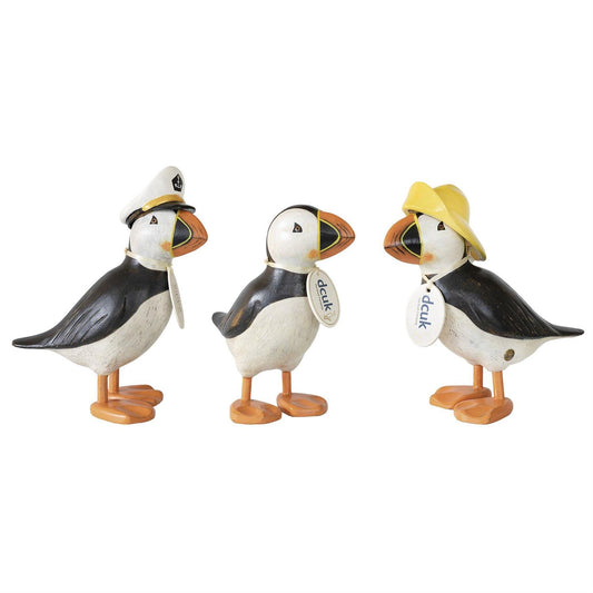 The Enesco DCUK Painted Puffins (6018579) set features three bamboo root puffins—one with a white captain’s hat, one plain, and one with a yellow rain hat. Each has orange feet and beak plus a charming name tag around its neck.