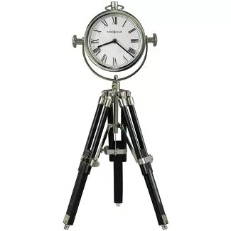 The Howard Miller Clock - Time Surveyor (635-211) features a round, silver frame with Roman numerals and sits on a black and silver tripod stand, blending vintage elegance with telescope-inspired design.