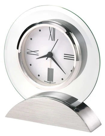 The Howard Miller Clock - Brayden (645-811) features a white face, black Roman numerals and hands, a silver frame with glass backing, and a curved metallic base—an elegant tabletop timepiece from Howard Miller.