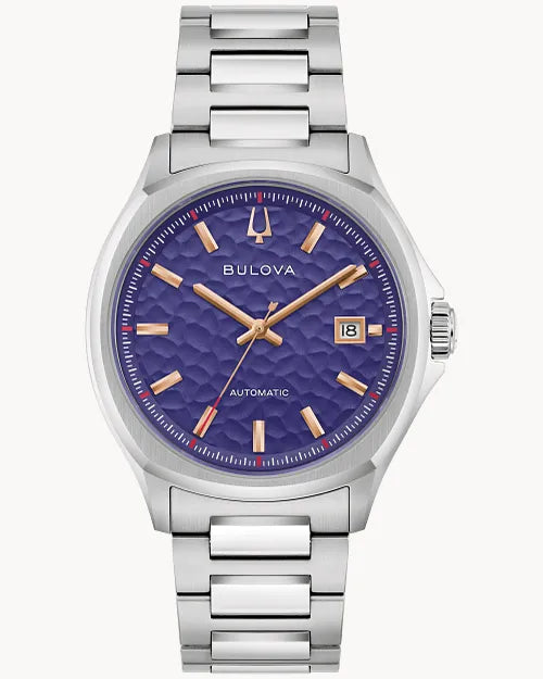 The Bulova Watch - Tony Bennett - 96B484 features a silver metallic band, textured purple dial, gold markers and hands, date window at 3 o’clock, and is an automatic men’s watch with "Bulova" on the face.