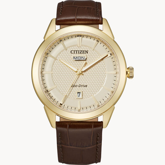 The Citizen Rolan AW0092-07Q Eco-Drive watch features a gold-tone case, beige dial with day-date display, gold markers and hands, CITIZEN and Eco-Drive branding, and a brown leather strap.