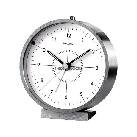 The Bulova Clock - Flair (B6844) is a silver round analog desk clock with a white face, luminous hands, and a slim black second hand showing 7:15:52, resting on a small rectangular base.