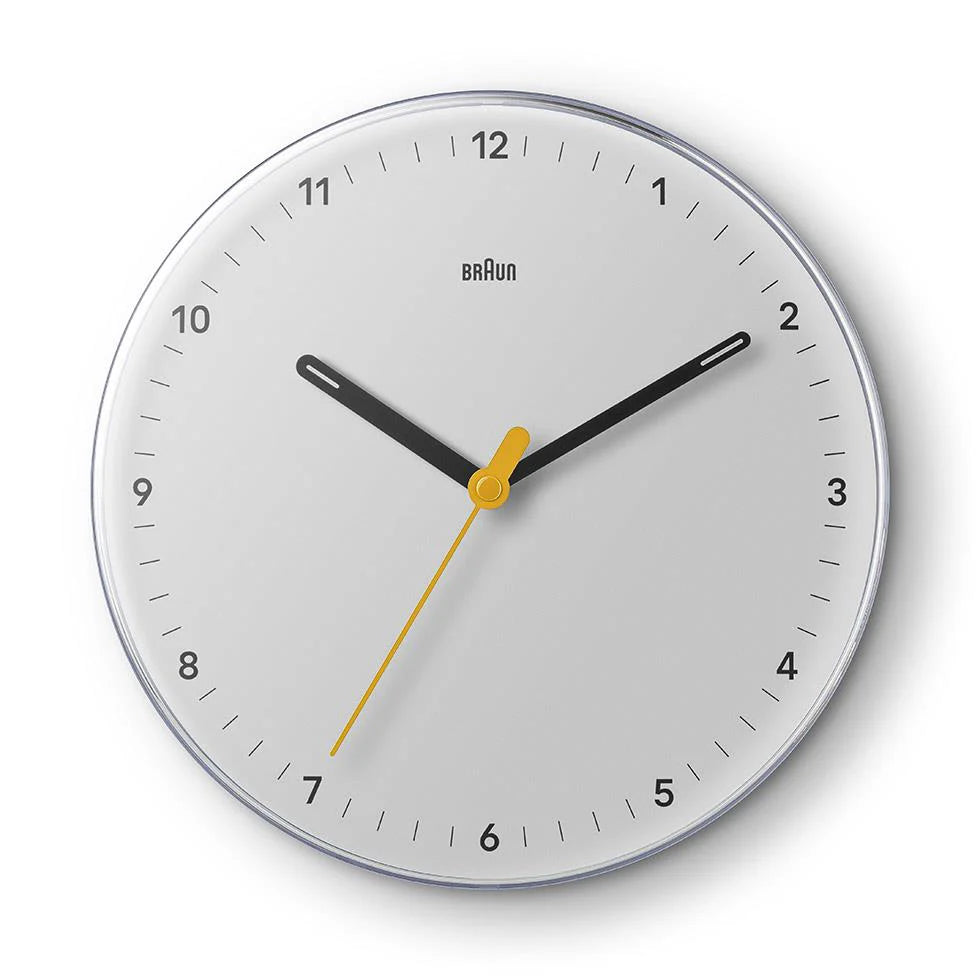 The Ameico Braun BC26W wall clock features a white face, black hour and minute hands, a yellow second hand, silent quartz movement, and simple black tick marks. The time shown is 10:20:33.
