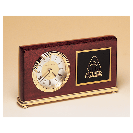 The JDS Desk Clock - Rosewood Piano Finish Clock (BC48) features a round gold-trimmed face, brass base, and an Arthritis Foundation logo plaque on the right, accented with elegant gold details.