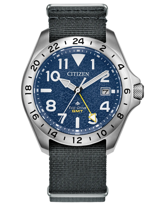 The Citizen Watch - Promaster Land GMT (BJ7150-09L) by Citizen features a blue textured dial, silver 24-hour bezel, white hour markers, date at 3 o’clock, and a gray fabric strap—perfect for any adventure.