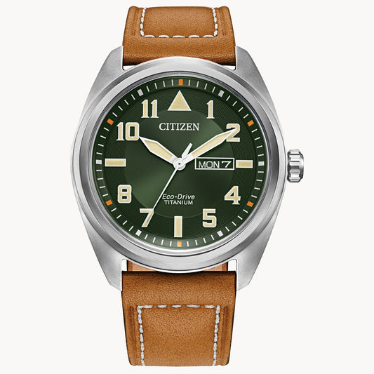 The Citizen Garrison Super Titanium (BM8560-02X) watch by Citizen features a green dial, luminous hands and markers, day-date display at 3 o’clock, and a brown leather strap with white stitching.