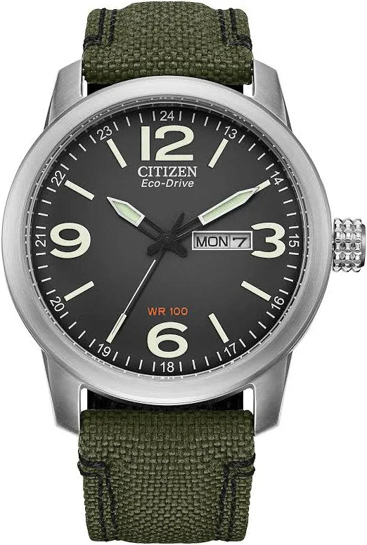 The Citizen Watch - Military Commemorative Box Set (BM8570-09E) features a black dial with large white numerals, day/date display, silver bezel, luminous hands, and a durable green fabric strap—a stylish men’s military watch by Citizen.