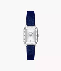 The Fossil Raquel ES5436 watch by Fossil features a rectangular silver case with diamond-studded bezel, white dial, minimal markings, and a dark blue leather strap, shown on a plain white background.