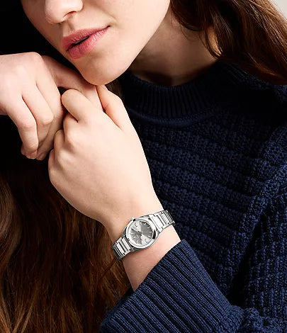 A person wearing a navy blue sweater rests their chin on their hands, highlighting the stylish Fossil Everett Watch (ES5490) by Fossil on their left wrist.