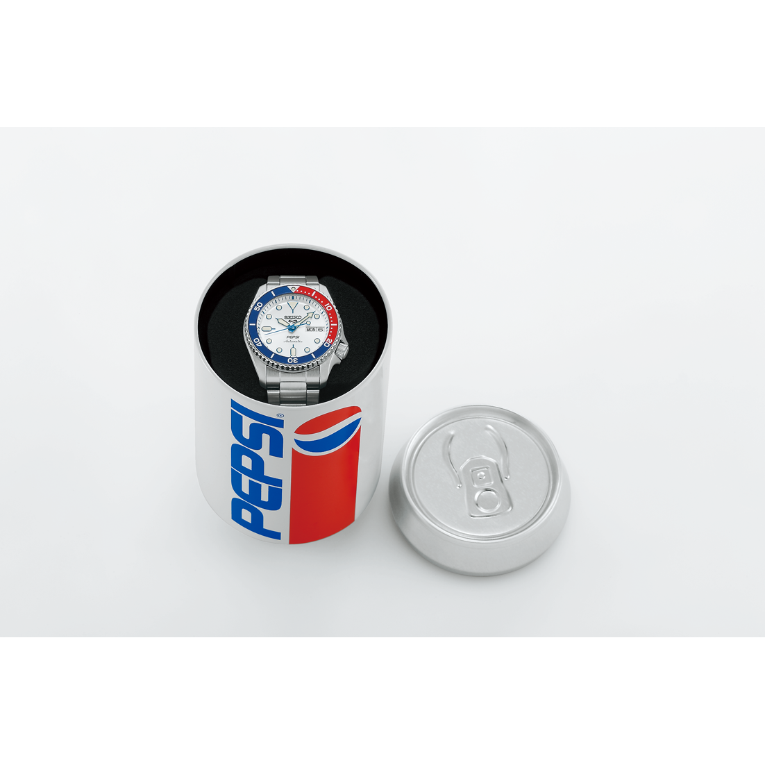 The Seiko 5 x Pepsi® Limited Edition SRPL99 automatic watch with a red, white, and blue bezel is displayed inside a round Pepsi can-style box, its lid off and set beside it.