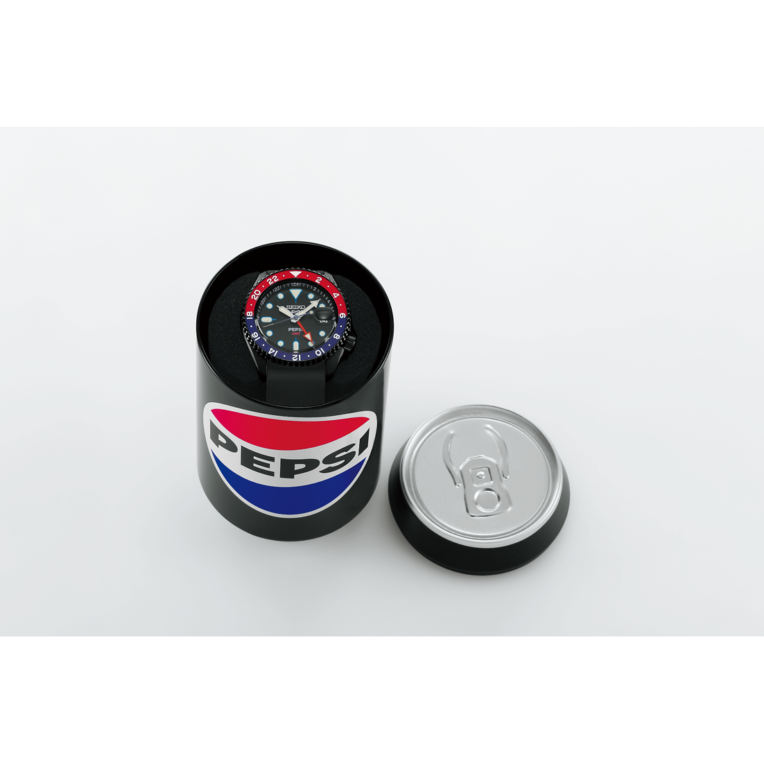 The Seiko 5 x Pepsi® Limited Edition SSK047 automatic watch with a red and blue bezel is displayed inside an open black can featuring the classic Pepsi logo, with the lid placed beside it on a white surface.