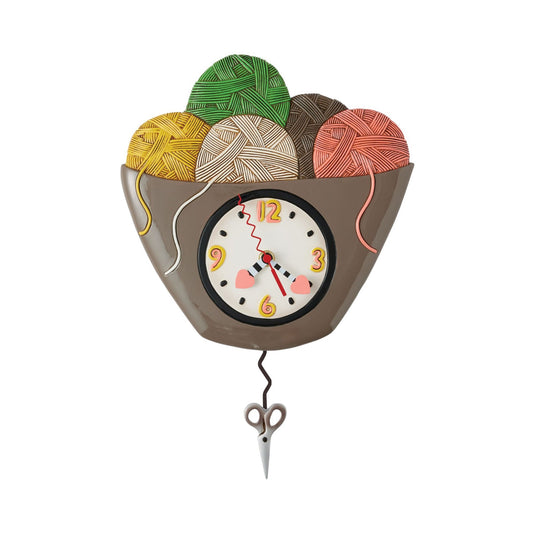 The Enesco Allen Designs Loose Ends Clock (6017294) features a bowl of colorful yarn balls, a cracked clock face, scissors as a pendulum, and yarn draped over the edge—perfect for craft lovers and unique decor.