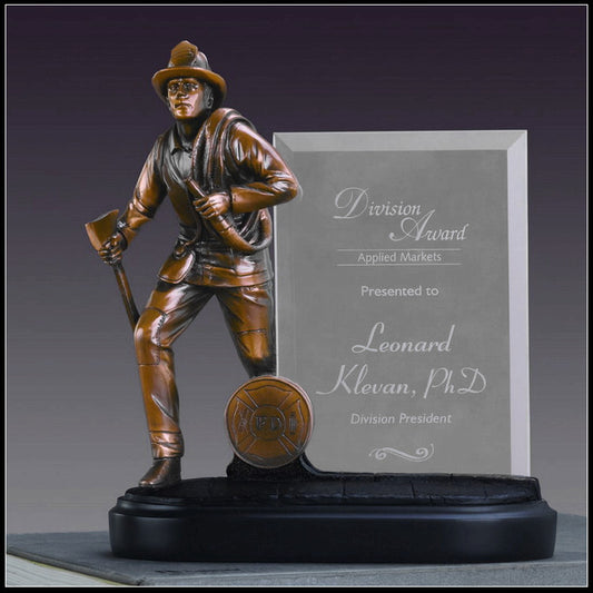 A Treasure of Nature Fireman Statue With Glass Plate For Engraving by Treasure of Nature features a firefighter with an ax beside a glass plaque engraved with “Division Award, Applied Markets, Presented to Leonard Klevan, PhD., Division President.”.