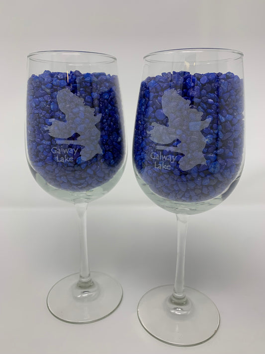 The Time Square Clock Shop TS Wine Glasses - Custom Set of 2 features each wine glass etched with a leaping person and "Galway Lake," filled with small blue stones, shown against a plain white background.
