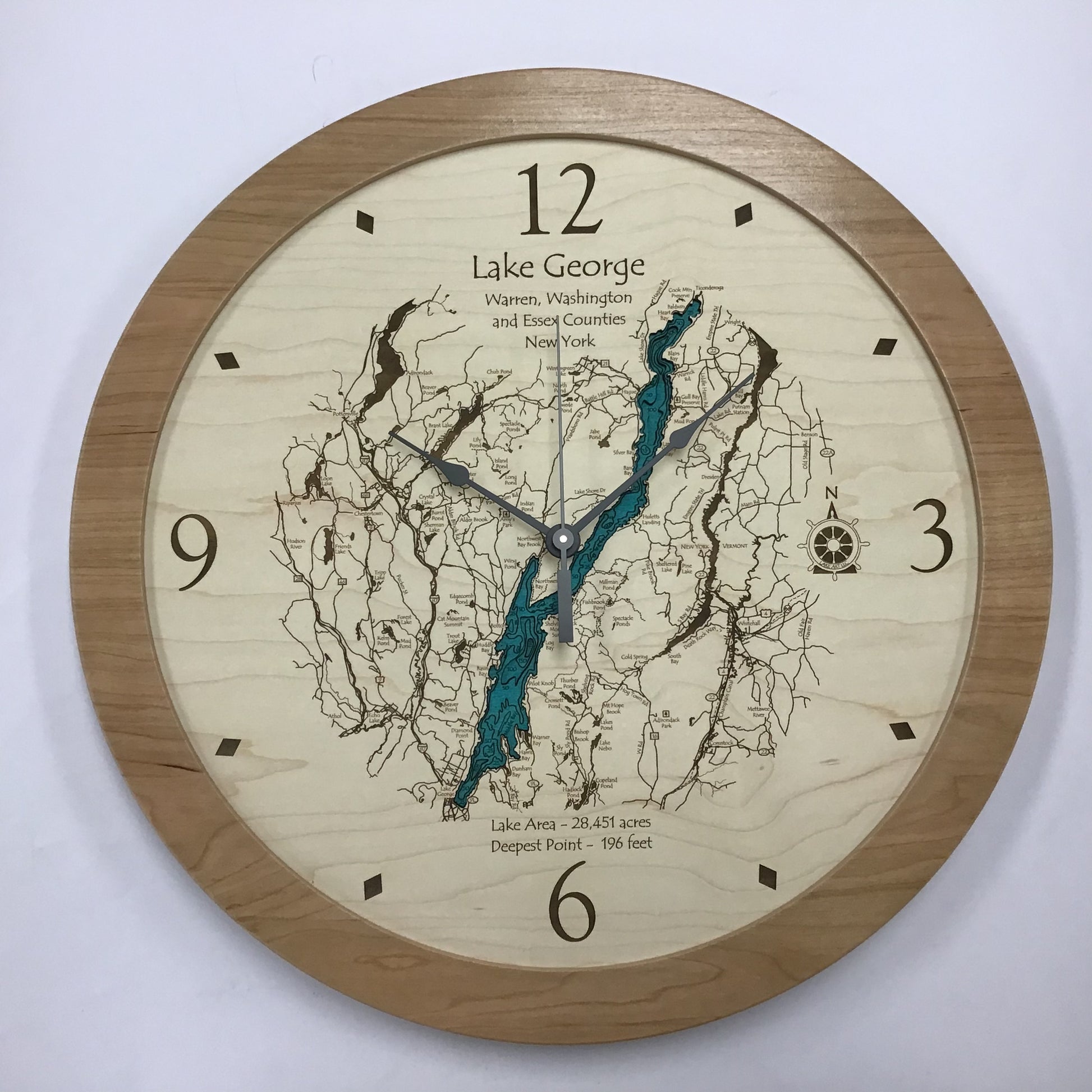 The Lake Art Clocks - Lake George Region Multi-level Clock by Lake Art is a round wooden wall clock featuring a detailed map of Lake George, NY at its center, with dark hands and numerals at 12, 3, 6, and 9 on a white background.