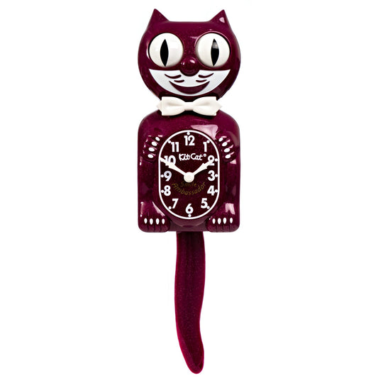 The California Clocks Kit-Cat Klock - Ruby Red Gent (BC-50) is shaped like a smiling cat with a white bow tie. Its eyes and tail are designed to move back and forth, and the clock face is centered on the cat’s belly.