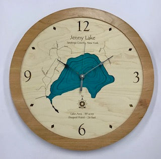 The Lake Art Clock - Jenny Lake NY by Lake Art is a round clock with a wooden frame, featuring an engraved map of Jenny Lake, Saratoga County. Its face shows blue lake details at the center, and the hands are set to 12:02.